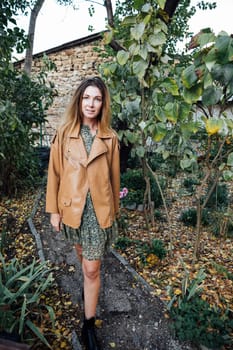 woman in a brown jacket walks in a park on the street