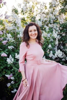 beautiful woman in a pink dress stands near a large lilac bush