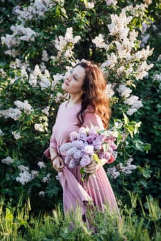 a woman in a pink dress by lilac bushes posing for a walk photo shoot