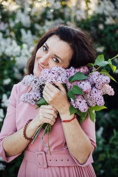 beautiful woman in a pink dress stands with lilacs in her hands