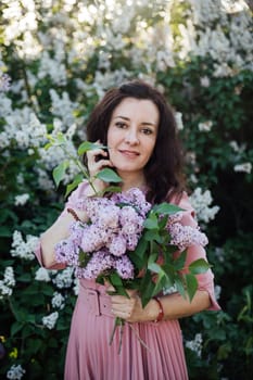 beautiful woman in a pink dress stands with lilacs in her hands