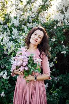 beautiful woman in a pink dress stands with lilacs in her hands