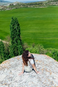 a woman sitting on a mountain nature green field look to the side