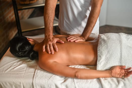 hispanic brunette adult fit woman enjoy massage by physiotherapist in the therapeutical bed at the spa
