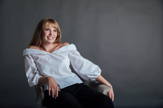 beautiful woman in a white shirt sits on a chair with a gray background