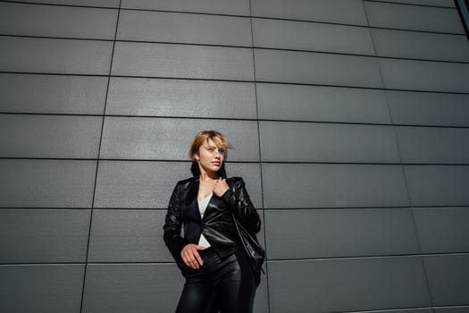 fashionable woman in leather black clothes stands against a graphic wall