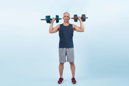 Full body length shot active and sporty senior man lifting dumbbell during weight training workout on isolated background. Healthy active physique and body care lifestyle for pensioner. Clout