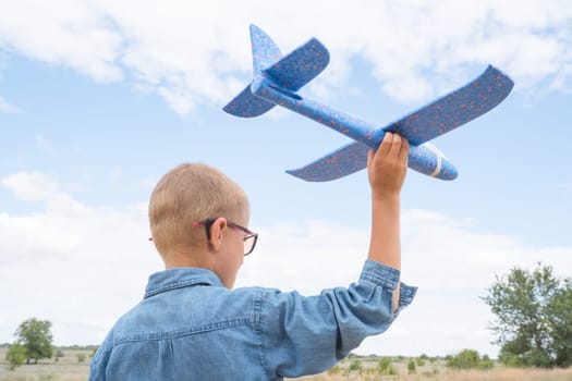 Portrait of a happy child playing with a toy airplane against a blue sky in an open field.