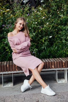 blonde woman sitting on bench by green bushes