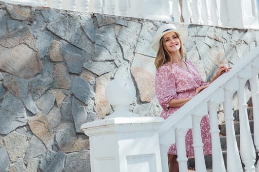 blonde in a hat stands at the white railing on the steps near the house walk on the street