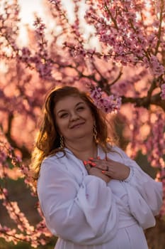 Woman blooming peach orchard. Against the backdrop of a picturesque peach orchard, a woman in a long white dress enjoys a peaceful walk in the park, surrounded by the beauty of nature