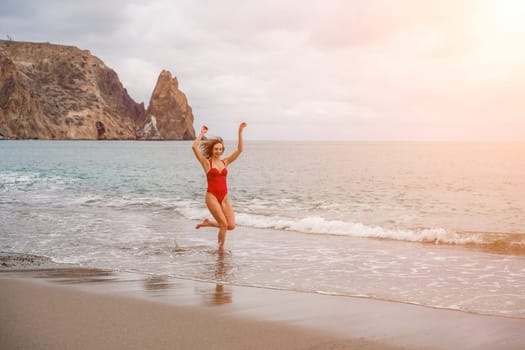 A beautiful and sexy brunette in a red swimsuit on a pebble beach, Running along the shore in the foam of the waves.