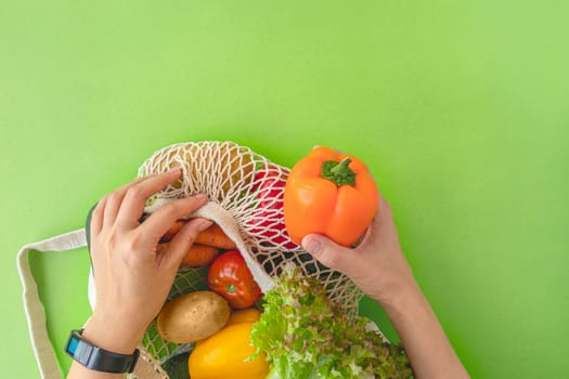 top view of a woman's hands taking vegetables out of an eco-bag. tomatoes, cucumbers, bell peppers and lettuce in a reusable bag. The concept of recycling, respect for nature. flat lay, copy space.