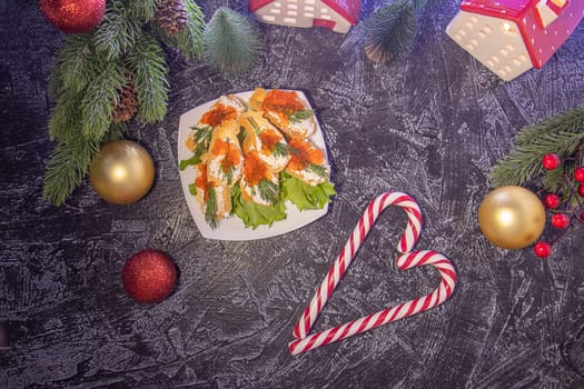 flat lay appetizer croutons with cream cheese and red caviar on a black textured background with Christmas tree branches and Christmas balls and candy sticks. serving for a Christmas party or New Year