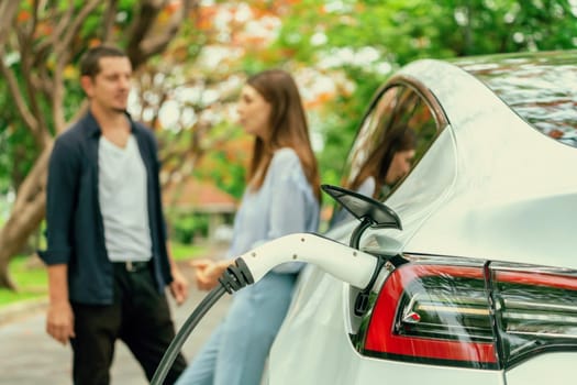 Lovely young couple recharging battery for electric car during autumnal road trip travel EV car in autumnal forest. Eco friendly travel on vacation during autumn. Exalt