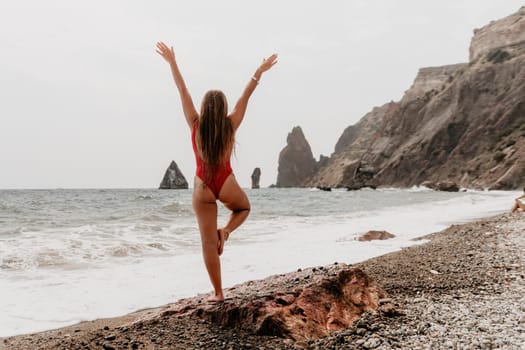 Woman sea yoga. Back view of free calm happy satisfied woman with long hair standing on top rock with yoga position against of sky by the sea. Healthy lifestyle outdoors in nature, fitness concept