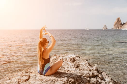 Woman sea yoga. Back view of free calm happy satisfied woman with long hair standing on top rock with yoga position against of sky by the sea. Healthy lifestyle outdoors in nature, fitness concept.