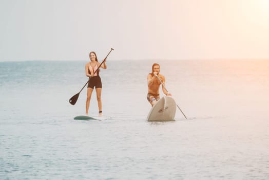 Sea woman and man on sup. Silhouette of happy young woman and man, surfing on SUP board, confident paddling through water surface. Idyllic sunset. Active lifestyle at sea or river