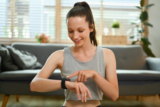 Satisfied sporty caucasian lady checking fitness tracker during workout at home.