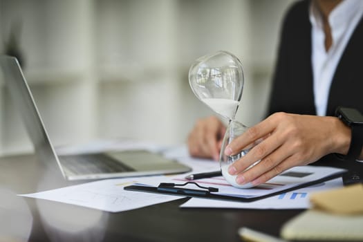 Professional businessman with hourglass sitting at office desk. Business and time management concept.