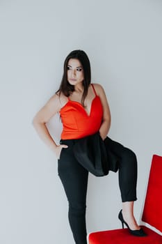 brunette woman stands by a red chair with a jacket in her hands