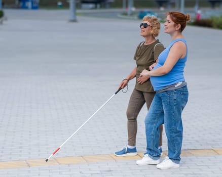 Caucasian pregnant woman leading blind elderly lady outdoors