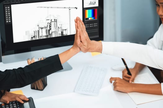 Diverse group of civil engineer and client celebrate and high five after make successful agreement on architectural project, reviewing construction plan and building blueprint at meeting table.Prudent