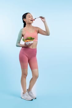 Young sporty Asian woman in sportswear holding salad bowl fill with vibrant of fruit and vegetable. Natural youthful and fit body lifestyle with balance nutrition on isolated background. Vigorous