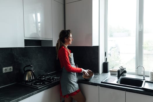 woman cook in an apron prepares food and looks out the window