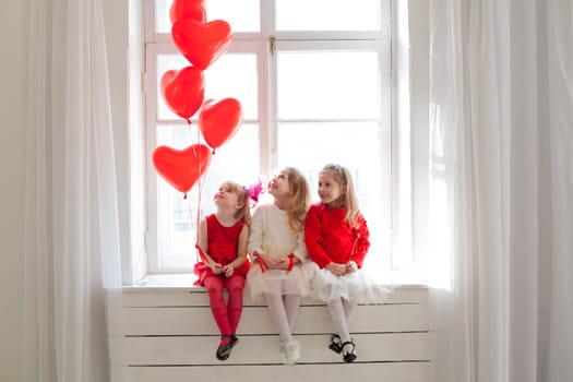 three girls sitting on the windowsill with red balls of the heart of Valentine's Day
