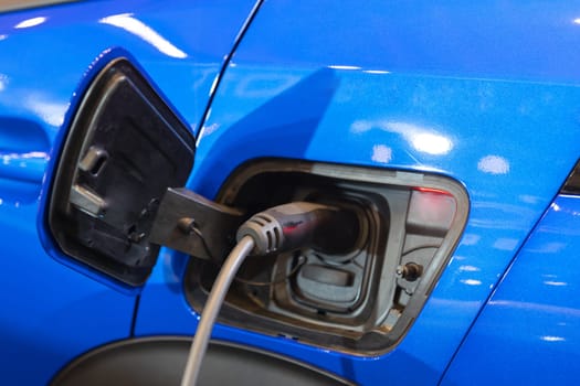 A blue car with an electric charger hooked up to it