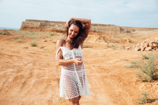 a woman in white clothes stands in a sandy locality