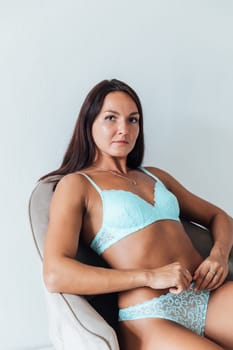 brunette woman in blue lingerie sits in a chair on a white background