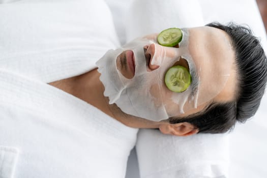 Serene daylight ambiance of spa salon, man customer indulges in rejuvenating with luxurious cucumber facial mask. Facial skincare treatment and beauty care concept. Quiescent