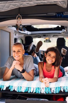 mother and daughter relaxing lying in the back of their camper van, concept of active tourism in nature and outdoor activities with children