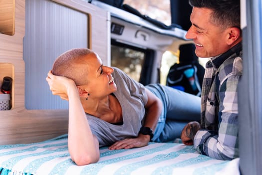 happy couple relaxing lying in the back of their camper van, concept of active tourism in nature and outdoor activities