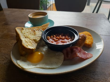 Full English breakfast with beans and sausage served on wooden table in pub