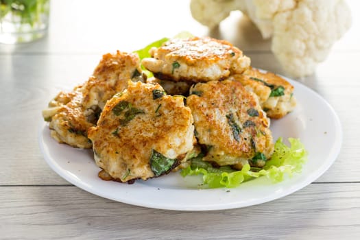 cooked vegetarian fried cauliflower cutlets, in a plate on a wooden table.