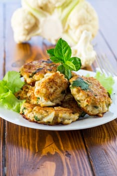 cooked vegetarian fried cauliflower cutlets, in a plate on a wooden table.