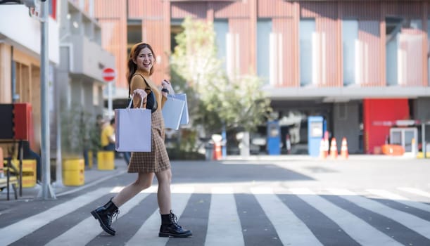 Beautiful Asian woman holding shopping bags and smiling while shopping on Black Friday outside the mall.