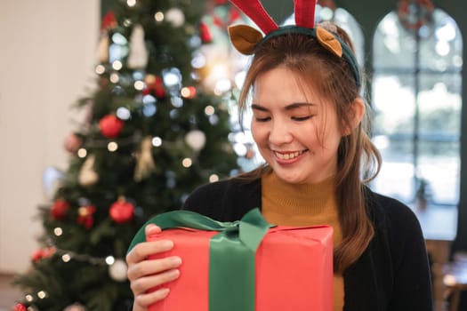 christmas time Adorable young woman with Santa hat and attractive and beautiful gift box for Christmas party in yellow long sleeve shirt near Christmas tree at modern home.