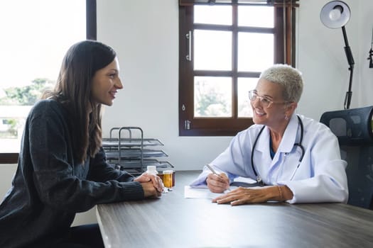 Elderly female doctor in white coat talking with beautiful young patient in clinic, giving advice on heart disease treatment and health care and medicine, medicine concept.