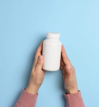Two female hands holding a white plastic bottle for pills on a blue background
