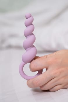 Close-up of a female hand with lilac anal beads lying in bed
