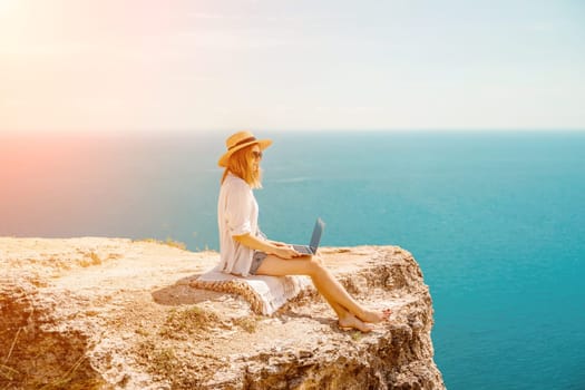 Freelance woman working on a laptop by the sea, typing away on the keyboard while enjoying the beautiful view, highlighting the idea of remote work