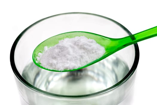 Spoon of baking soda over glass of water, isolated on white