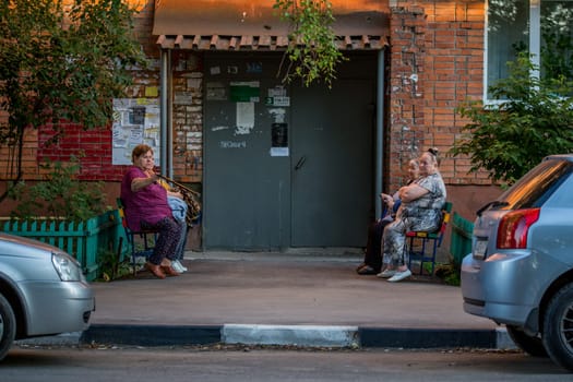 grandmothers sitting on benches in front of apartment building entrance and chatting in Tula, Russia - June 27, 2018