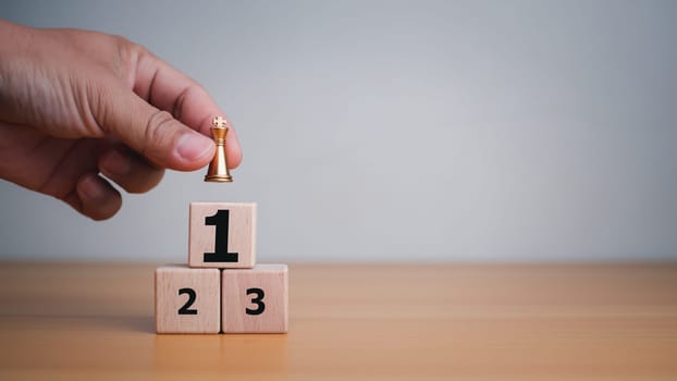 Businessman hand holding a king placed on the topmost layer of wood. It represents the concept of competition and strategic adjustments for competitors in the business.