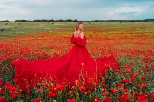 Woman poppy field red dress. Happy woman in a long red dress in a beautiful large poppy field. Blond stands with her back posing on a large field of red poppie