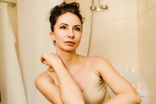 Portrait of a middle-aged woman, smiling with her arms folded in front of her face, her hair pulled up. The brunette is in a good mood. On a light background